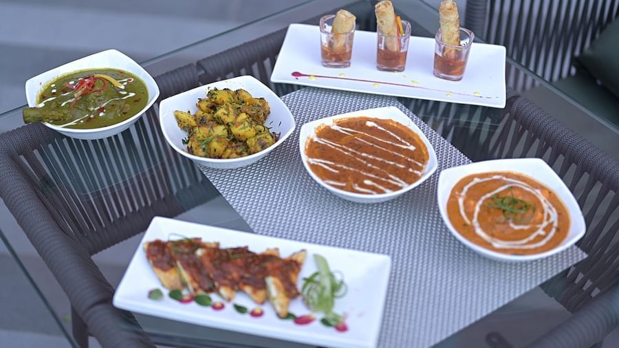 A tabletop arrangement of several small dishes of Indian cuisine, including curries, vegetables, and appetisers, presented on white serving ware. - Clarks Safari Haridwar