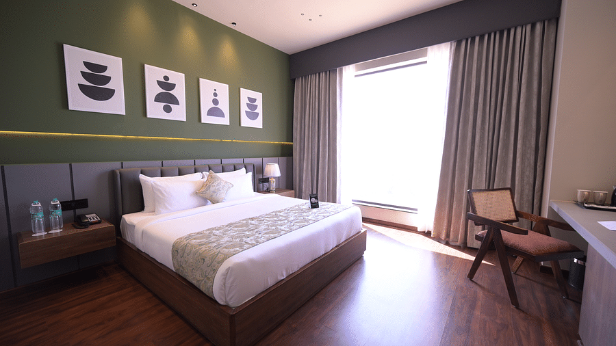 Deluxe Room featuring a king size bed, minimalist decor, and a large window with curtains. - Clarks Safari Haridwar