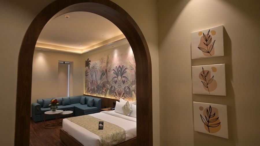 A view through an arched doorway revealing a bed, seating area, and decorative wall art, complemented by three framed pictures on the wall on the outside in Premium Room. - Clarks Safari Haridwar