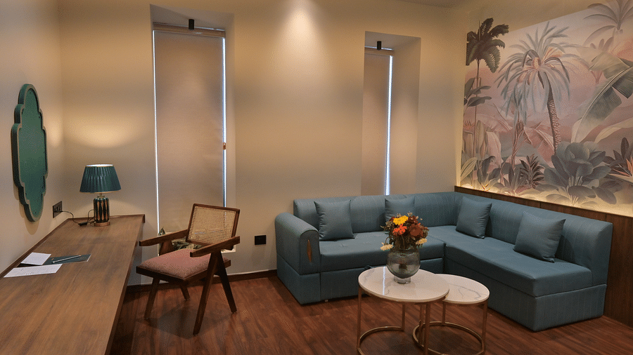 A cosy living room area with a corner sofa, a small coffee table, a desk with a chair, and a decorative wall mural in Premium Room. - Clarks Safari Haridwar