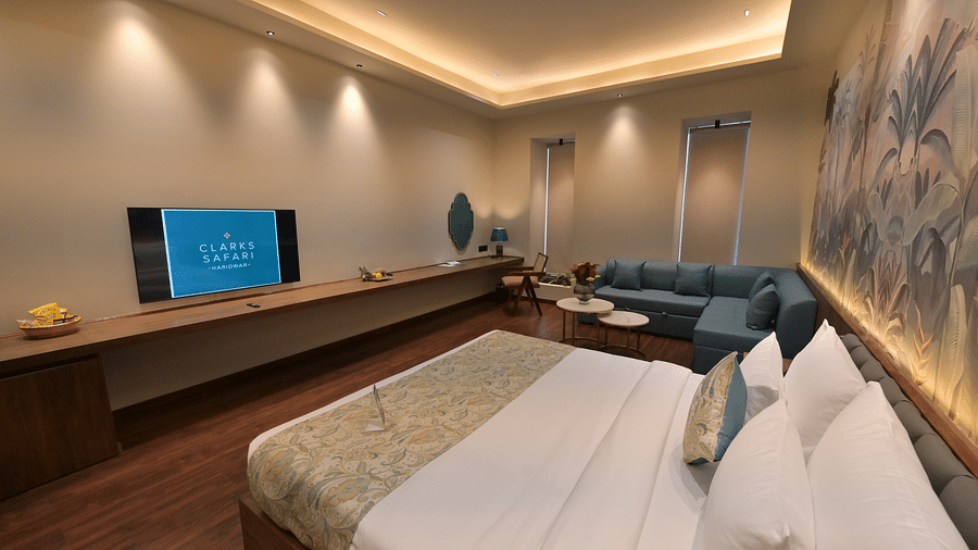 Premium Room featuring  a king size bed, a long console with a television, and a seating area with a blue sofa. - Clarks Safari Haridwar