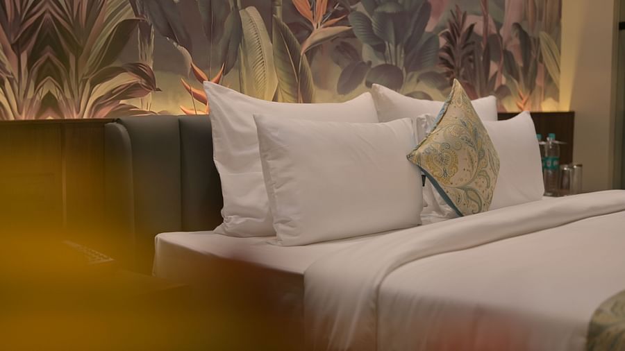 A neatly made bed with white linens and pillows, with a decorative leafy wallpaper backdrop in Premium Room. - Clarks Safari Haridwar