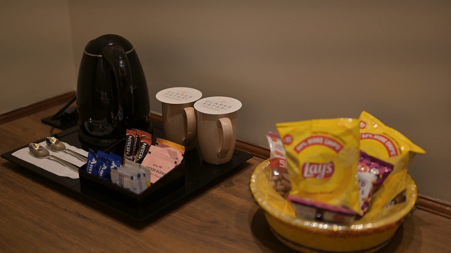 A refreshment setup including a kettle, cups, spoons, and snacks in bowls in Premium Room. - Clarks Safari Haridwar