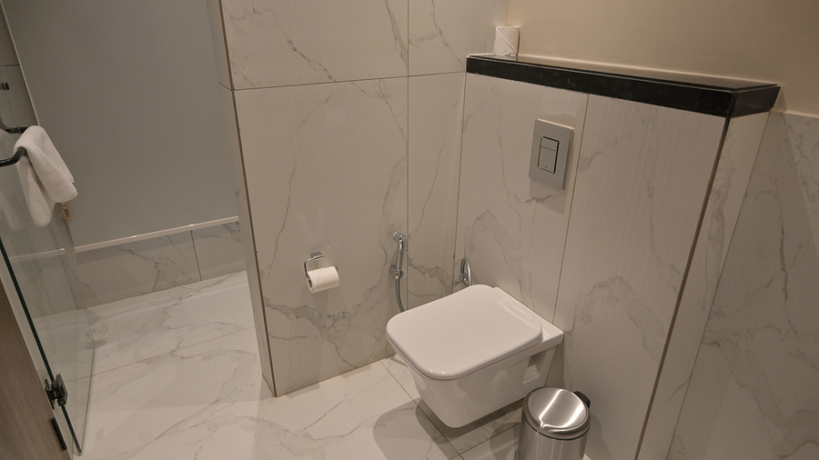 A clean, modern bathroom featuring a toilet, a small trash can, and white tiling of Premium Room. - Clarks Safari Haridwar