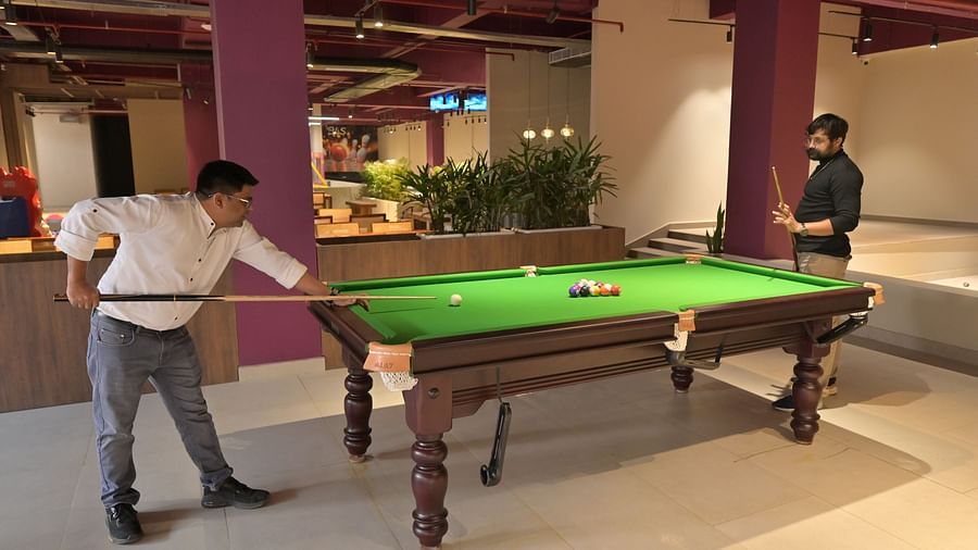 Two men playing snooker around a snooker table, the room having indoor plants in small bushes here and there - Clarks Safari, Haridwar