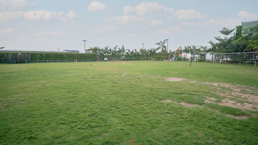 An expansive, flat green lawn at Clarks Safari Kheda, stretching towards the horizon, with distant structures under an open sky.