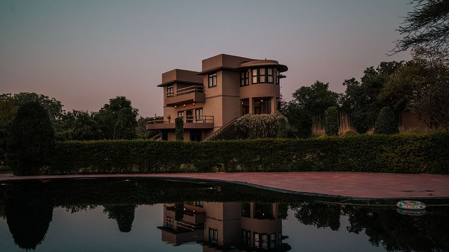 Stone building with multiple windows reflected in a still body of water. Trees and dusk sky in the background create a serene atmosphere - Clarks Safari, Pushkar