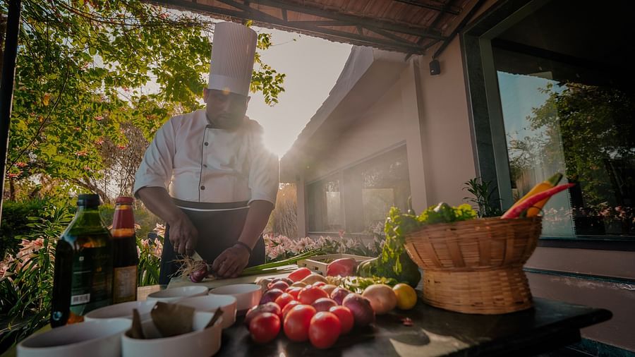 Outdoor cooking station with various ingredients including vegetables, herbs, and spices. Sunlight streams in from the side - Clarks Safari, Pushkar
