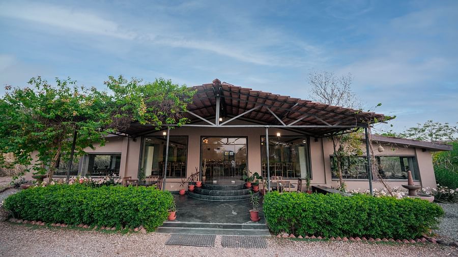 Here's an alt text option for the image, keeping it relevant, descriptive, and under 200 characters:  Modern, single-story building with a distinctive pitched roof and open entrance. Green bushes line the front, and trees are visible on either side under a