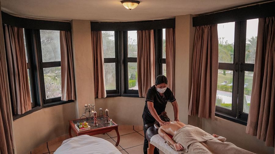 Luxurious hotel room featuring a grand arched window with curtains and an outside view. A neatly made bed and a figure in dark clothing are present - Clarks Safari, Pushkar