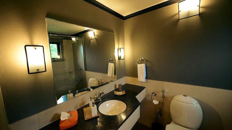 Bathroom of Deluxe King Cottage at Clarks Safari Pushkar featuring a large mirror mounted on the wall over a sink and a toilet next to it under warm lighting
