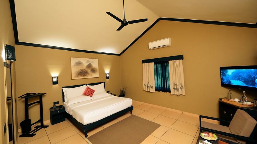 Deluxe King Cottage at Clarks safari Pushkar featuring a plush bed near the window and a TV mounted on the wall in front of it next to a sitting space 