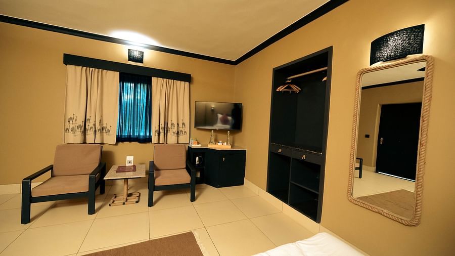 Sitting space in Deluxe Twin Cottage at Clarks Safari Pushkar by the window with a TV on the wall behind the chairs with a wardrobe and a large mirror on one side