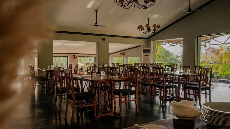 Interior view of the restaurant with wooden chairs and large windows offering natural light.  | Clarks Safari Pushkar