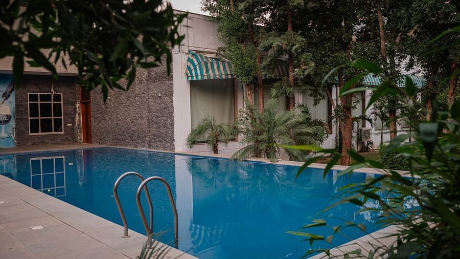A pristine turquoise swimming pool reflects the surrounding white buildings and lush greenery on a sunny day - Clarks Safari, Ranthambore