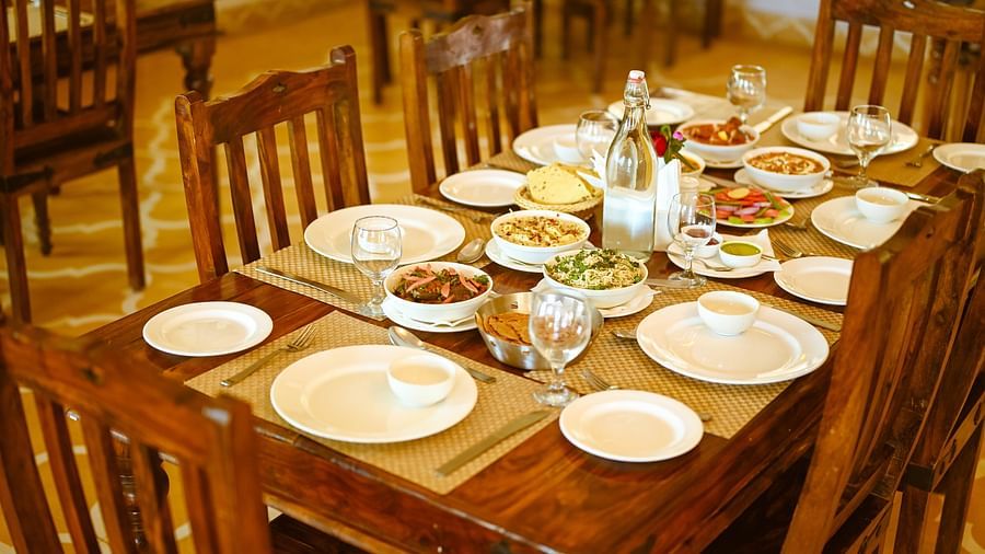 A dining table set with food, plates, and wine glasses at Clarks Safari, Ranthambore.