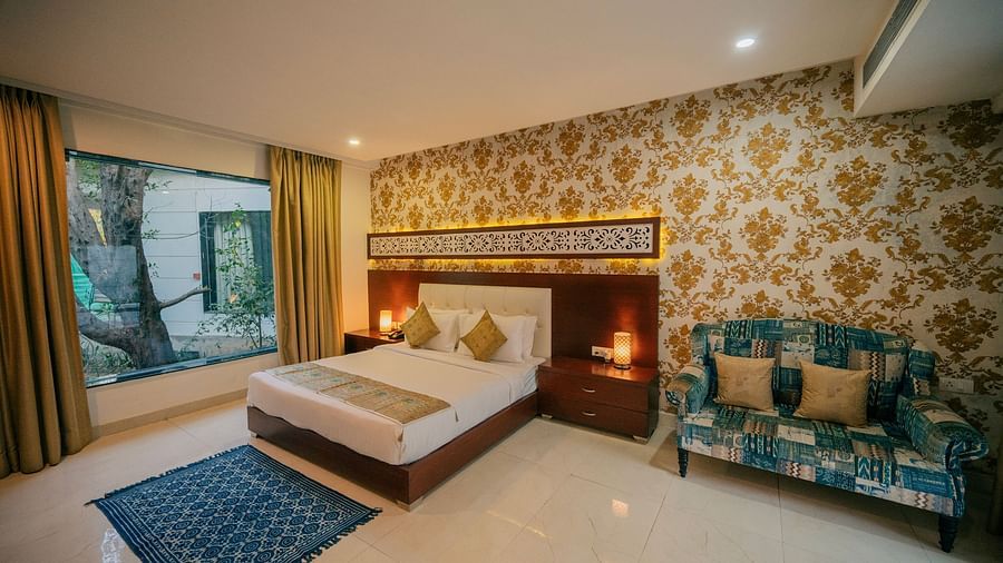 Elegant hotel room with ornate gold wallpaper, a king-size bed with decorative pillows, a patterned blue rug, and a comfortable sofa - Clarks Safari, Ranthambore