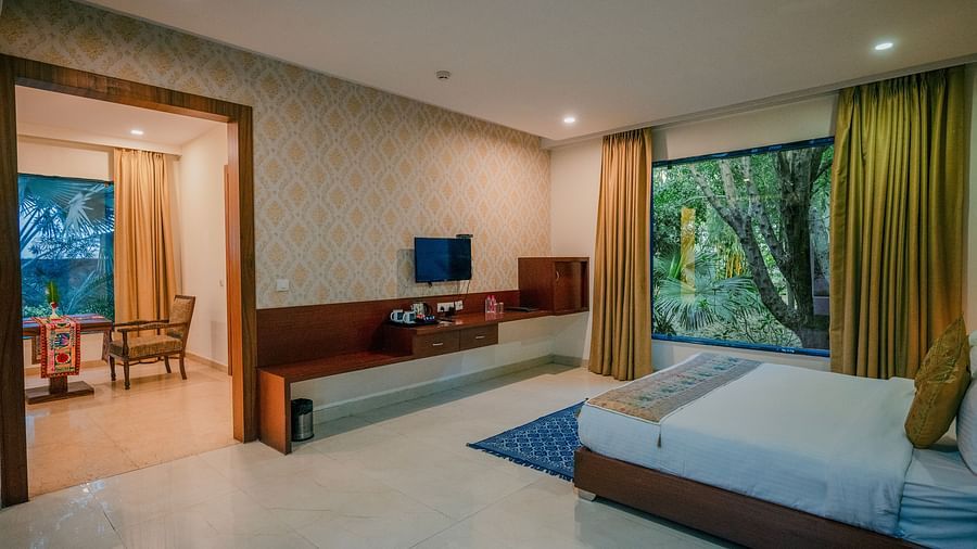 Spacious hotel suite with a king-size bed, a separate living area with a sofa, and large windows offering ample natural light - Clarks Safari, Ranthambore