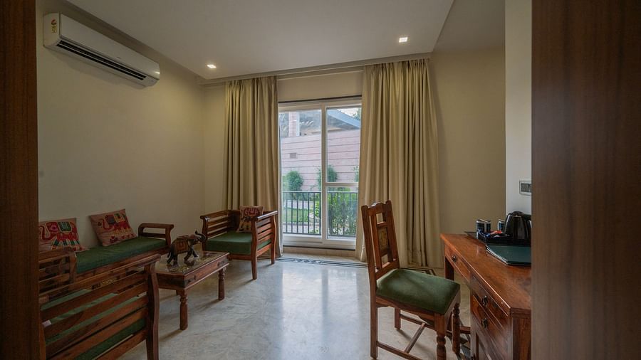 Bright and airy living room with a wooden dining table and chairs, a sofa, and large windows overlooking greenery - Clarks Safari, Ranthambore