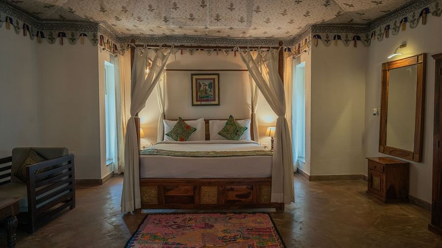 Comfortable bedroom with a four-poster bed adorned with patterned fabric, bedside tables with lamps, and a colourful rug on the floor -  Clarks Safari, Ranthambore