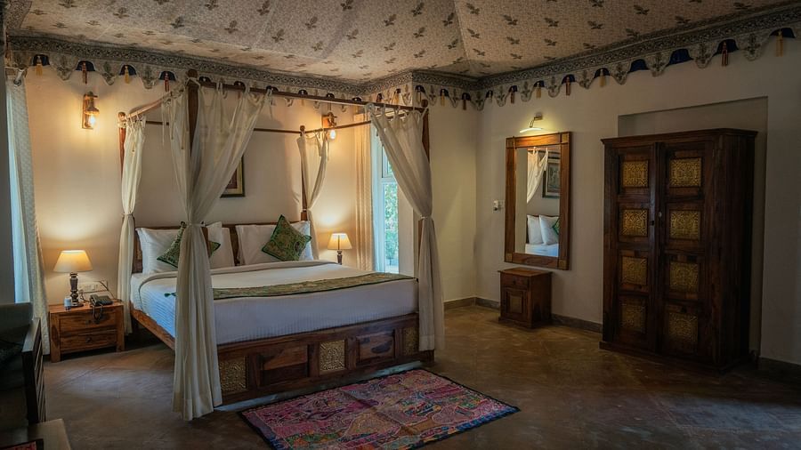 Elegantly decorated bedroom featuring a four-poster bed with white linens, a wooden wardrobe, and soft lighting, accented by a patterned rug - Clarks Safari, Ranthambore