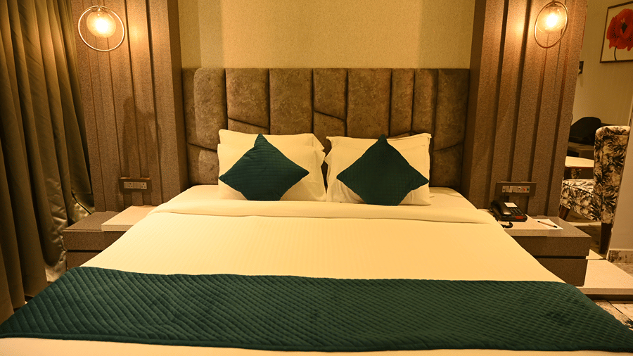 Deluxe Room at HM Resort with a wooden bed, green cushions, a dark green bed runner, a floral patterned rug and warm wall sconces in the background.