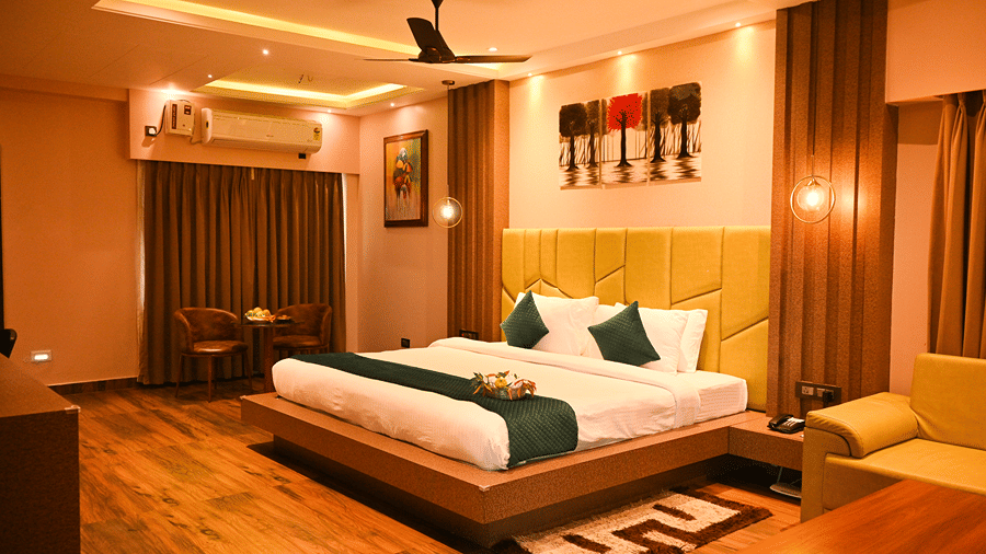 Semi Suite cottage with towel swans on the bed, an olive sofa, a wooden coffee table with fruit and a small dining set at HM Hotel & Resort, Dibrugarh.