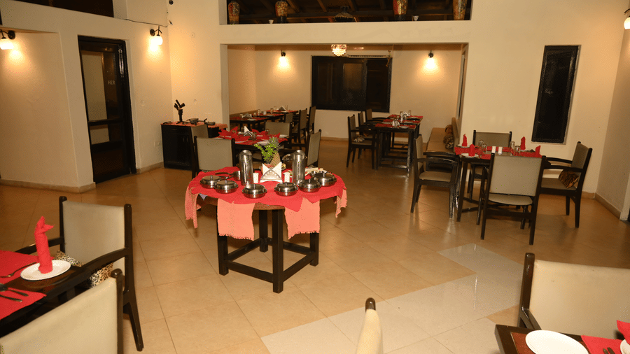 An indoor dining area with multiple tables, chairs, and a central table setup arranged for a special occasion at Infinity Resorts Bandhavgarh.