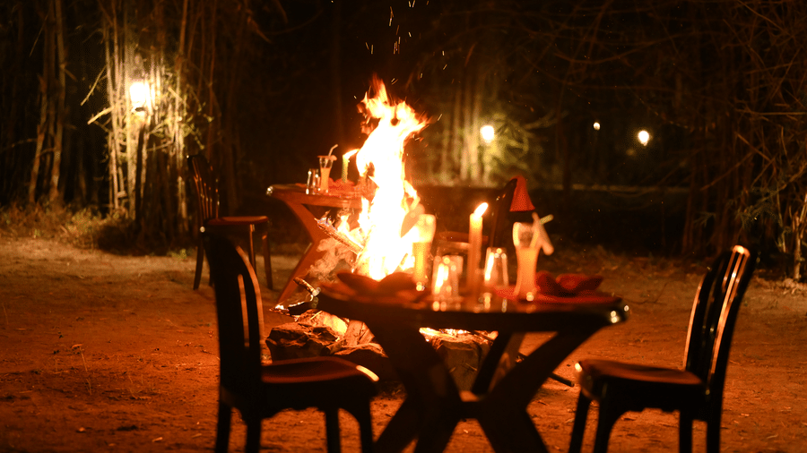 An outdoor bonfire setup with chairs placed around a fire pit on open ground at Infinity Resorts Bandhavgarh.