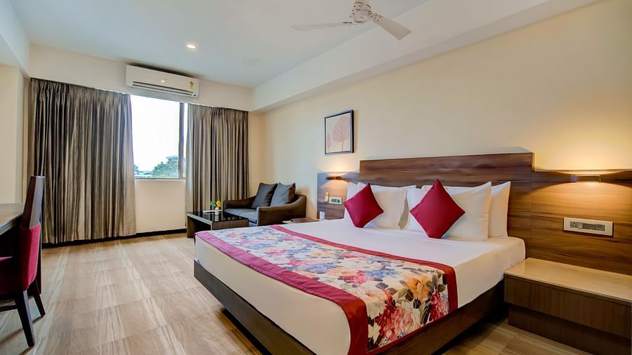 Spacious room with a double bed, lounge chairs, and natural light from large windows at Voyage Milestone Hotel and Banquet Siliguri