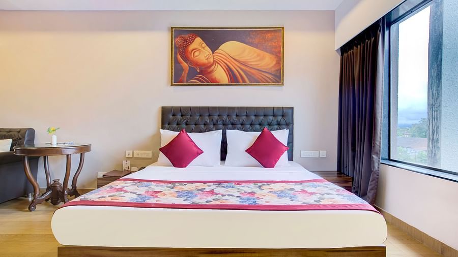 Elegant bedroom featuring a vibrant bedspread, wall art, and a large window with city views at Voyage Milestone Hotel and Banquet Siliguri