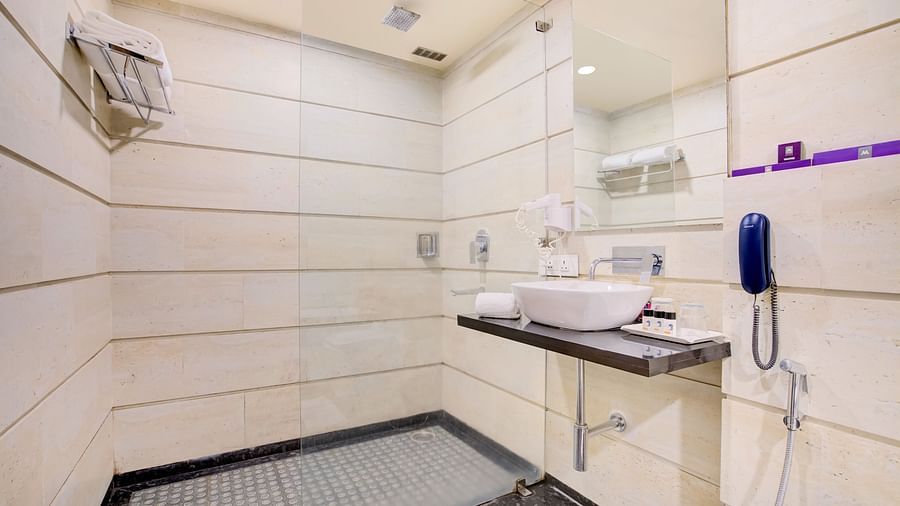 Modern bathroom with sleek white tiles, a wall-mounted sink, hair dryer, and minimalist design at Voyage Milestone Hotel and Banquet Siliguri