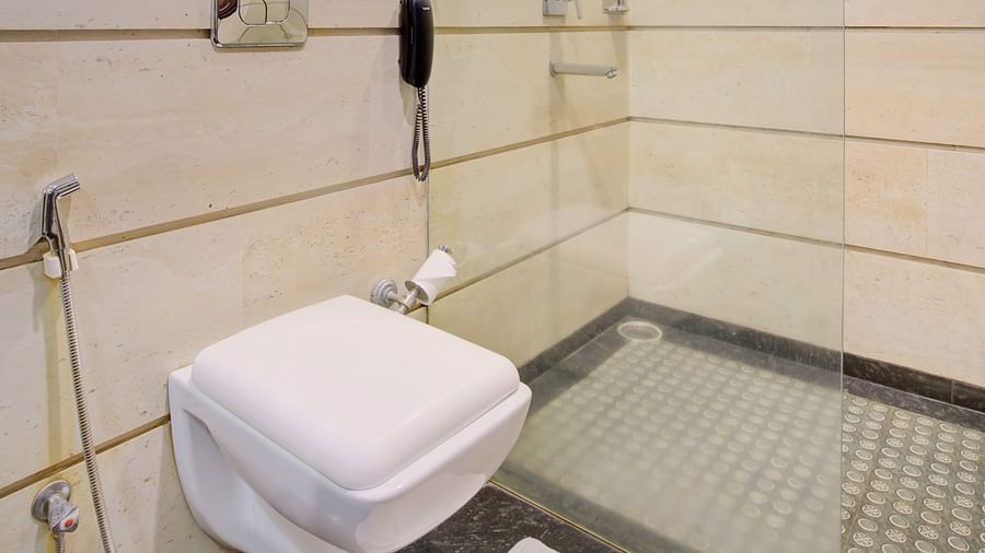 Compact bathroom with a wall-mounted toilet, handheld bidet, and tiled walls at Voyage Milestone Hotel and Banquet Siliguri