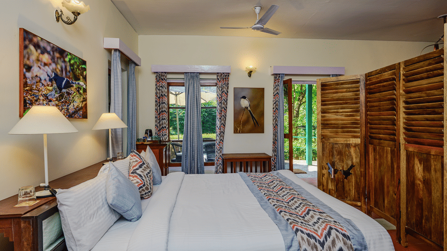 Bright heritage style bedroom with beds wooden furniture patterned textiles and ample natural light offering a restful stay at Neemrana’s Glasshouse on The Ganges suited for families or companions travelling together