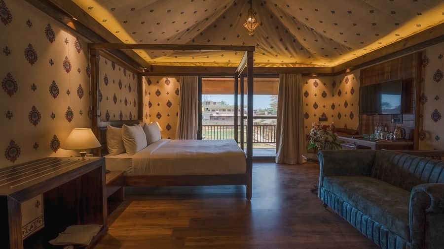 A Premium Duplex Tent featuring a poster bed, a sofa, a flat TV screen and a table beneath, a cabinet table, and a balcony attached at The Baagh Ananta Elite, Ranthambore
