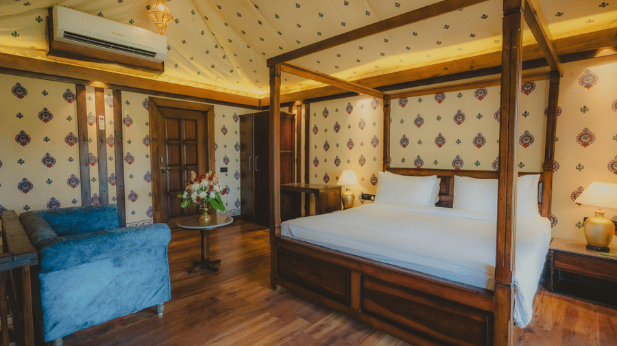 A Premium Duplex Tent bedroom featuring a sofa, a poster bed, bedside table with lamps on either side, cabinet table, a wardrobe, and a centre table with flower vase at The Baagh Ananta Elite, Ranthambore