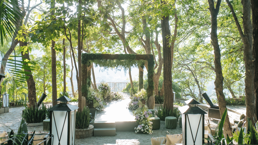 An event space at The Den Corbett Resort, with a decorated arch, flowers, and plants.