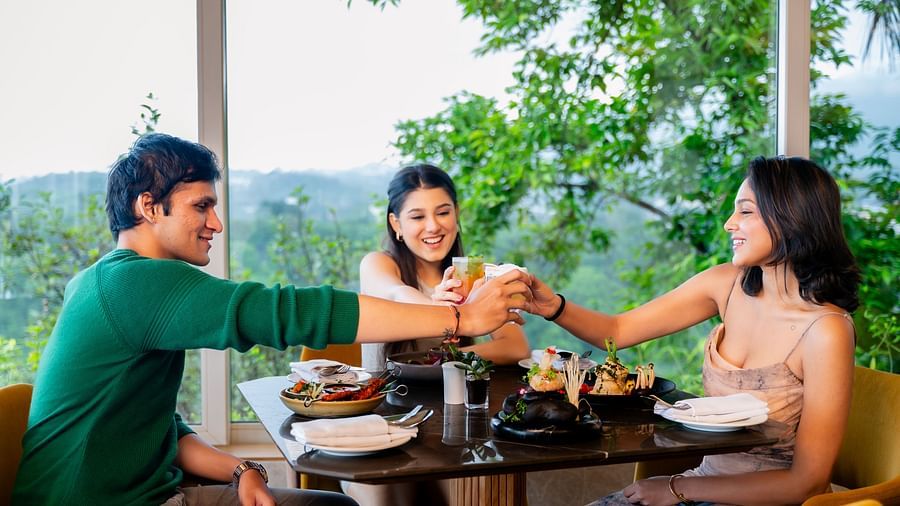 An image of three people sitting in a cafe clinging there glasses together with an amazing view behind them - The Dukes Retreat, Khandala
