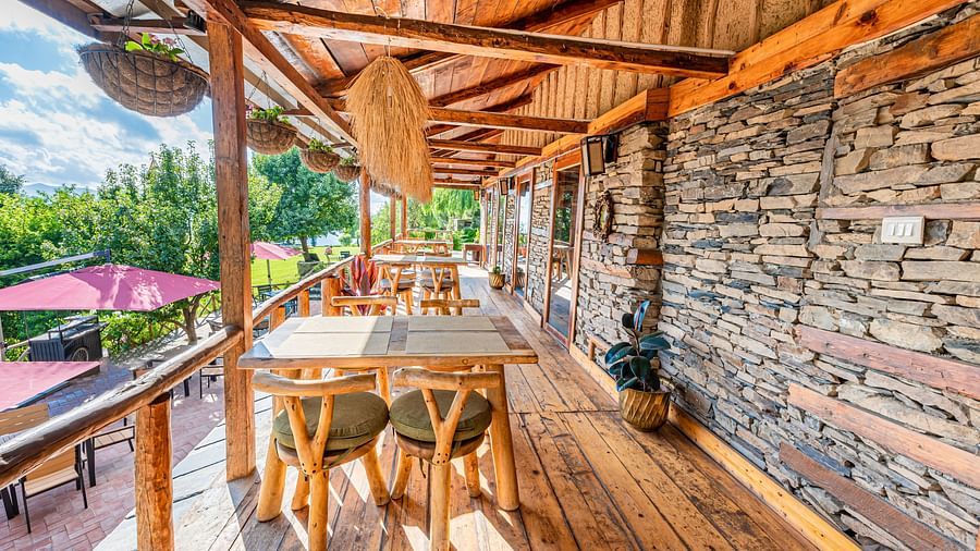 A balcony in Mario restaurant with wooden chairs placed in front of a limestone walls - The Manor Luxury Hotel, Shimla