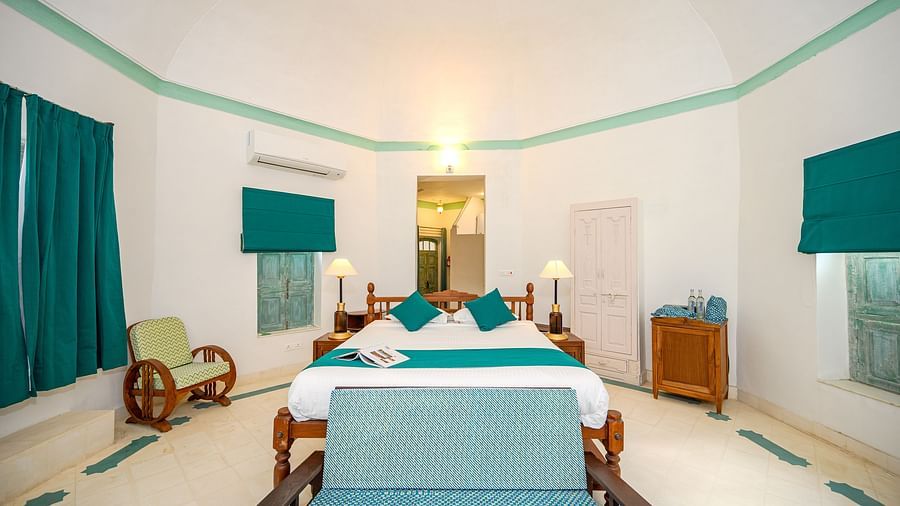 A long shot of a room with white walls and a table with a runner, chair in the centre and window on the left side with a blind on - Tijara Fort-Palace - 19th Century, Alwar