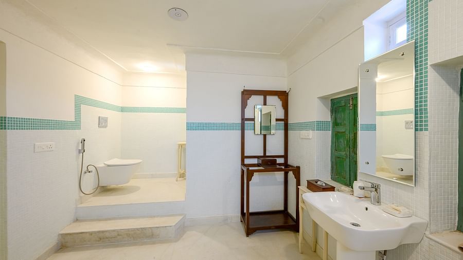 A bathroom with a sink, a mirror mounted to the wall, a window and a toilet in the background. - Tijara Fort-Palace - 19th Century, Alwar
