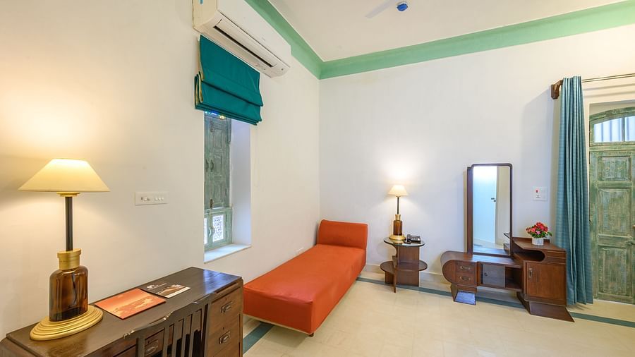 A bedroom with a wooden dresser, lamp, mirror, and a cushioned bench near the window. - Tijara Fort-Palace - 19th Century, Alwar