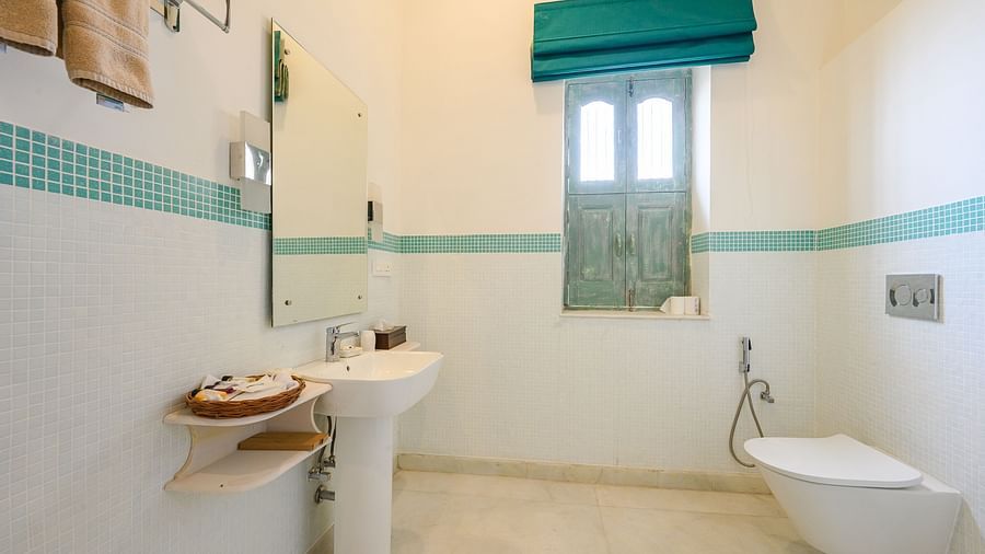 A side shot of a bathroom where a sink, toilet, mirror mounted on the wall, a window and a towel hanging from the towel rack. - Tijara Fort-Palace - 19th Century, Alwar