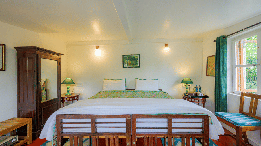Front view of the Camphor room at Wallwood Garden - 19th Century, Coonoor with a wooden bed, bedside tables, wardrobe and patterned rugs.