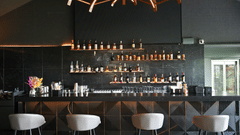 Modern bar at Hotel Daspalla, Hyderabad with black marble backdrop, premium spirit display on lit shelves, white bar stools, and curved wooden ceiling beams with warm lighting.