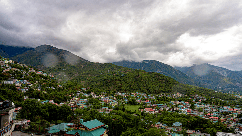 Aerial view of a hill town surrounded by lush green mountains under a cloudy sky.