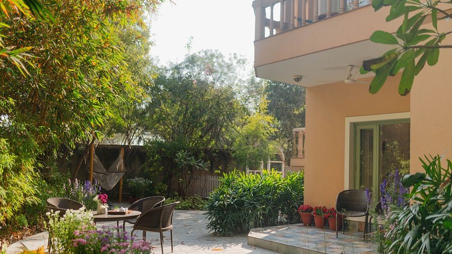 A garden view at Karma Chalets with patio chairs, table, and surrounding plants beside a building.