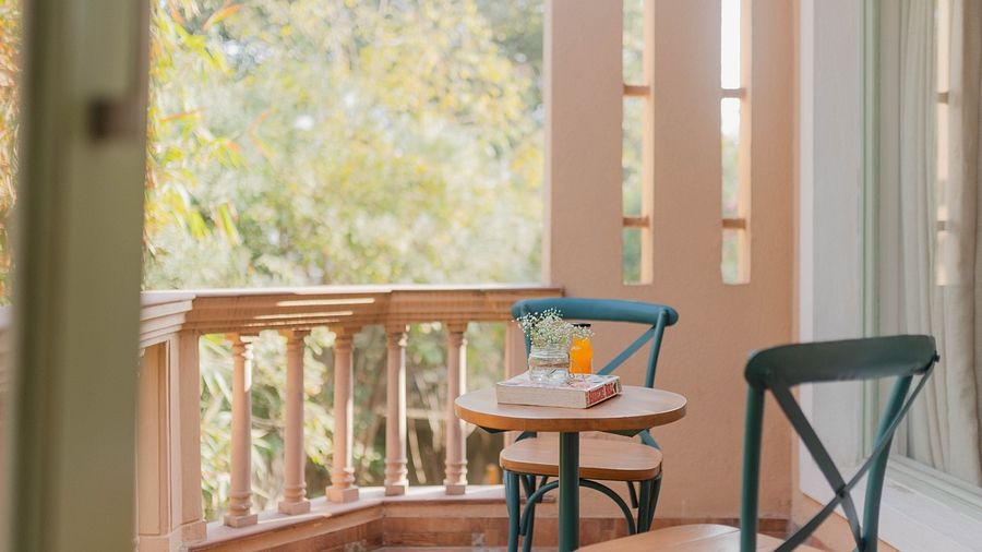 A balcony at Karma Chalets with a round table, two chairs, and wooden railing overlooking trees.