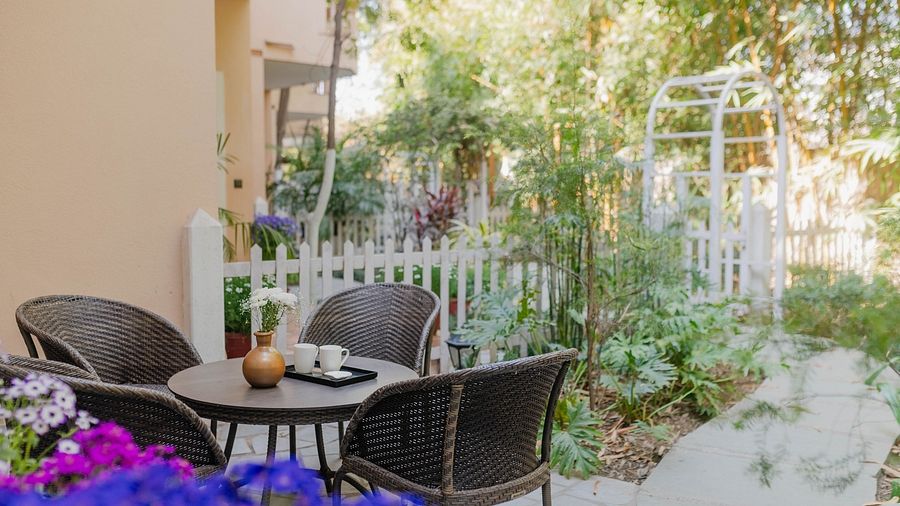 Outdoor seating at Karma Chalets with two black chairs, a table, flowers, and a white gate in the background.