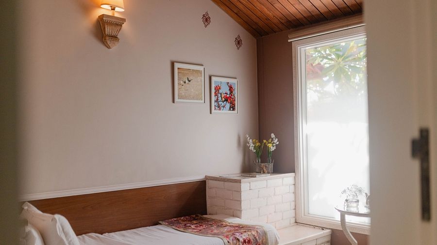 A single bed with a wooden headboard, framed pictures on the wall, and a window at Karma Chalets.